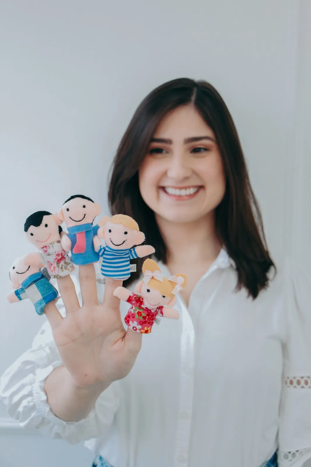 Bruna Rocha sorrindo e segurando fantoches de dedo usados na terapia infantil
